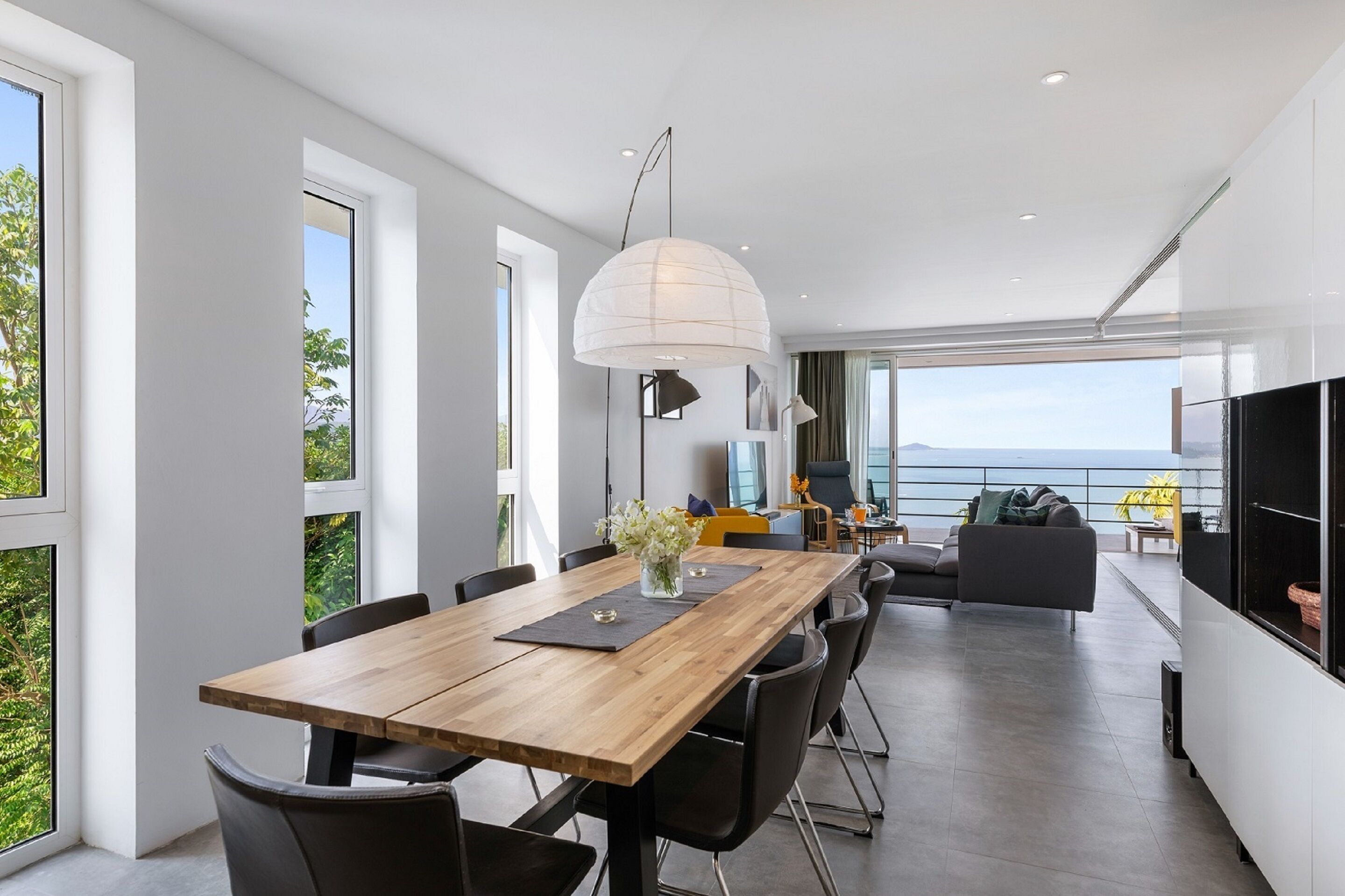 A modern dining area with a wooden table, black chairs, and a large white pendant light.