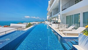 A modern hotel pool with clear blue tiles, lounge chairs, and a view of the ocean. - Luxury Apartment Unique Residences (Koh Samui)