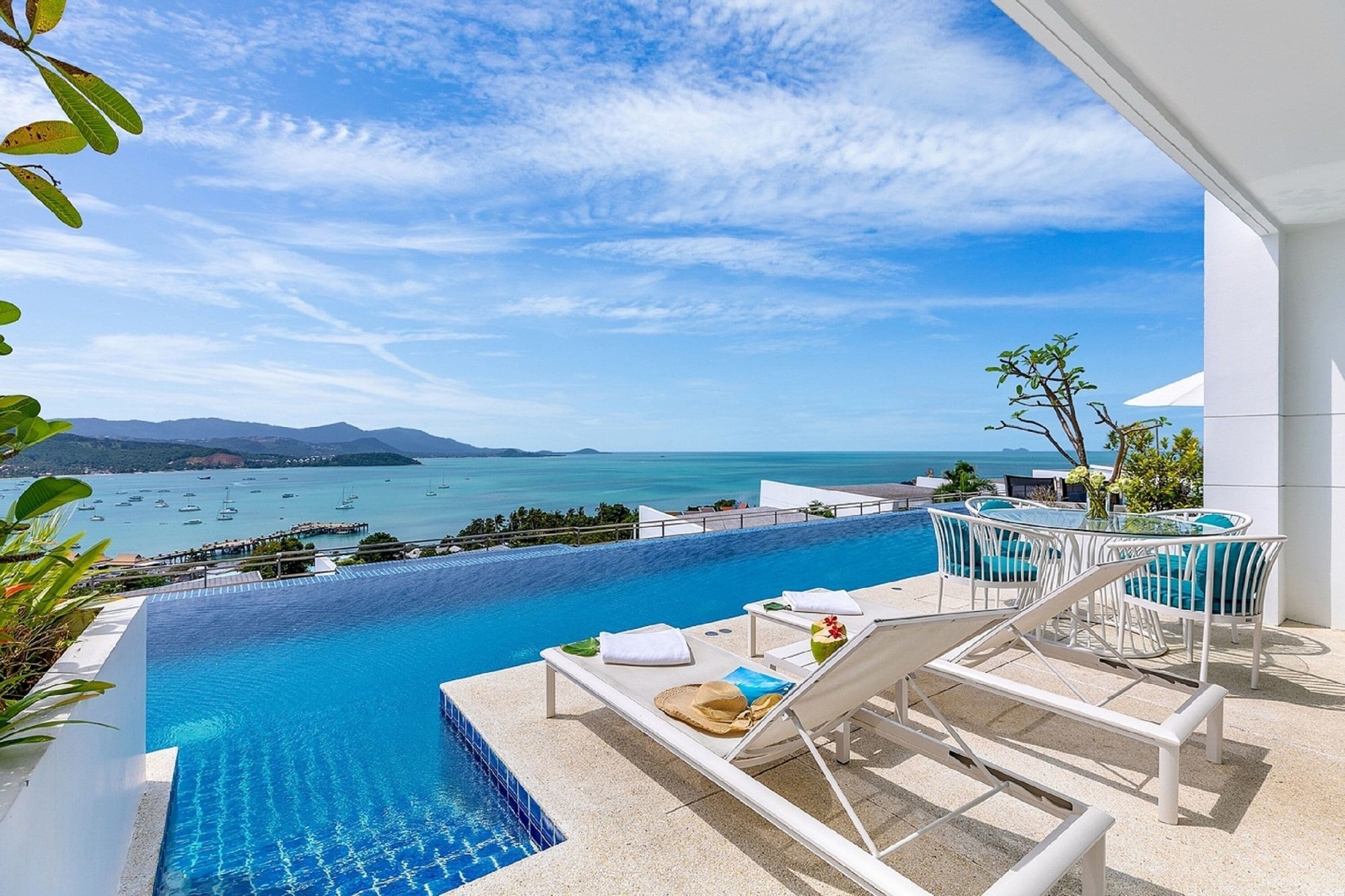 Ein Infinity-Pool mit Blick auf das Meer und die Berge. Liegestühle und ein kleiner Tisch mit einem Getränk sind ebenfalls vorhanden.