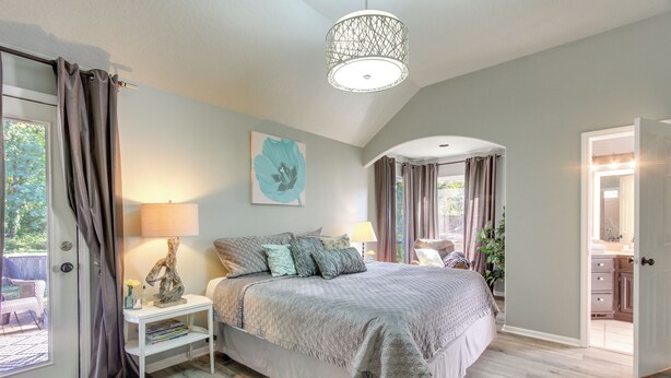 A bedroom with a large bed, a nightstand, a lamp, and a view of the outdoors.