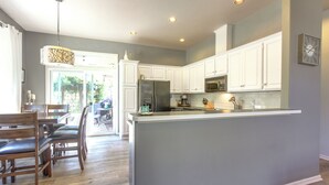 A modern kitchen with white cabinets, a central island, and a dining area with wooden chairs.