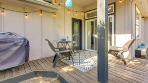 An outdoor patio with a covered grill, two wicker chairs, a small table, and string lights.