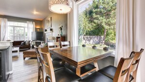 A modern kitchen with a dining area, large windows, and a view of the outdoors.