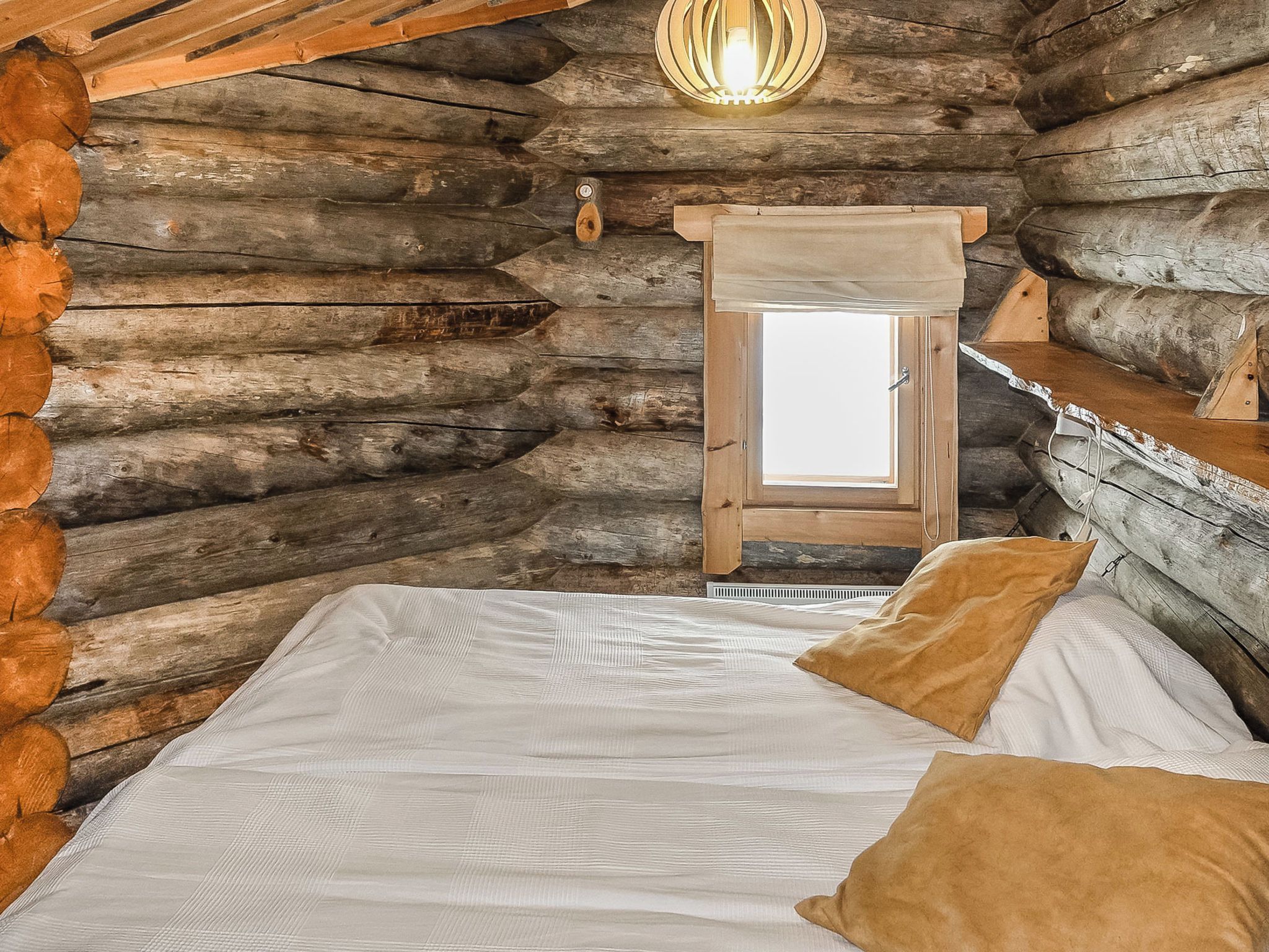 A log cabin bedroom with a bed, pillows, a wooden ladder, and a light fixture.