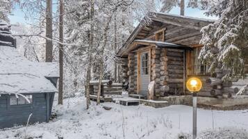 Uma cabana de tronco com varanda de madeira e um letreiro iluminado, rodeada por árvores cobertas de neve.