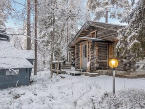 En timmerstuga med en träveranda och en upplyst skylt, omgiven av snötäckta träd.