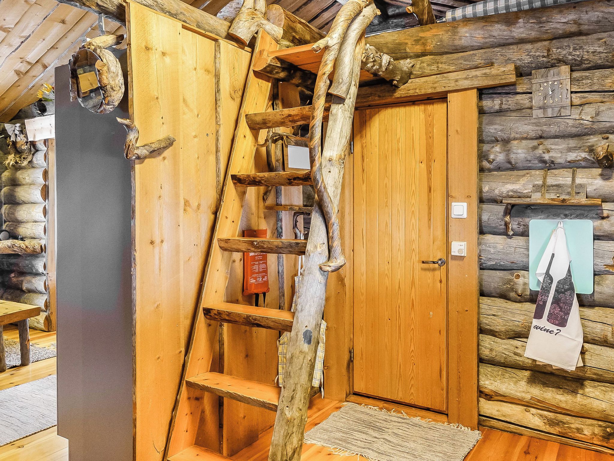 Un interno rustico in legno con una scala di legno che conduce a una zona soppalcata, una porta in legno e un porta asciugamani a parete.