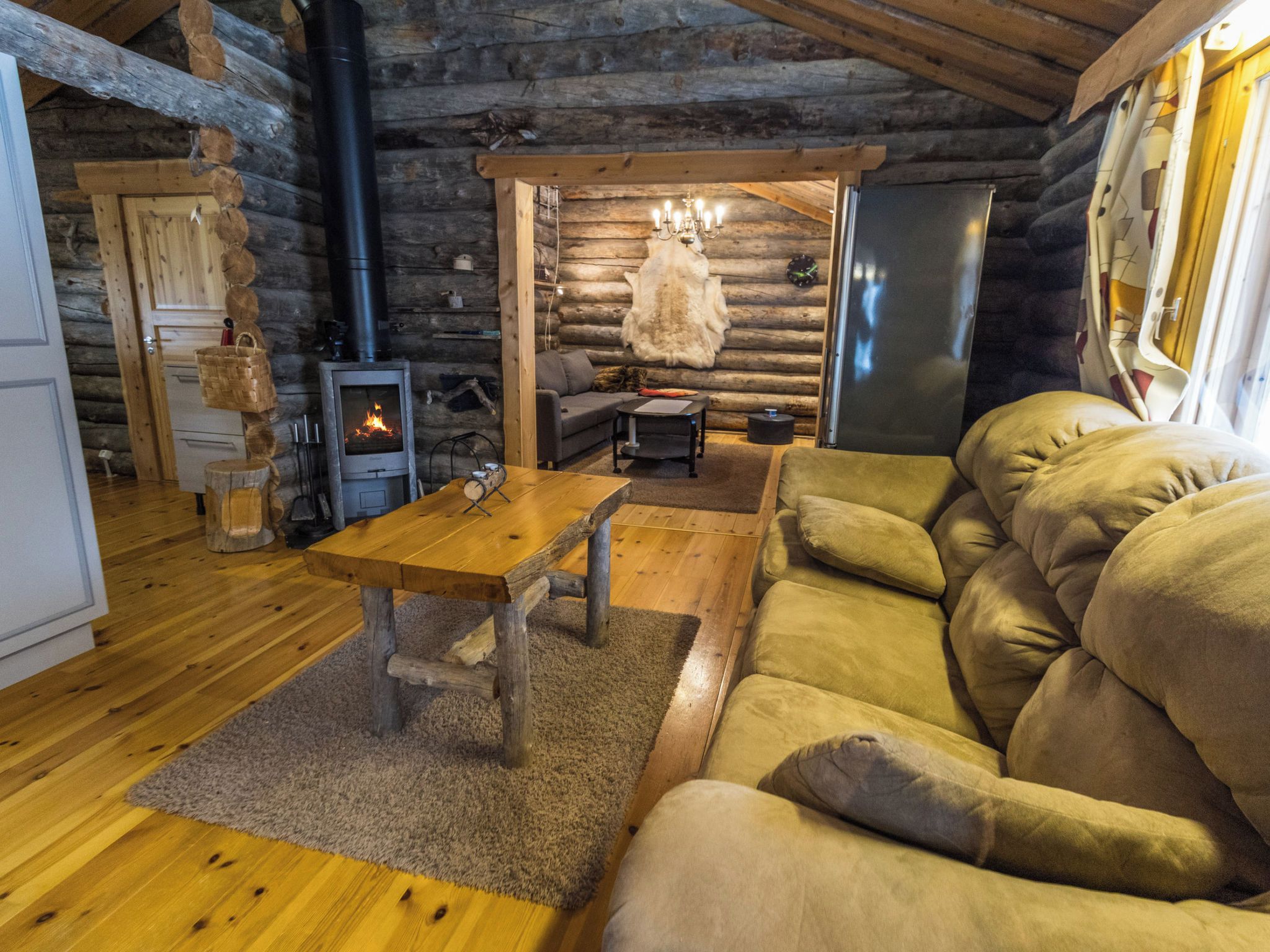Et interiør af en træhytte med et træbord, sofa og en brændeovn.