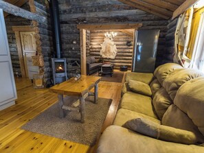 A log cabin interior with a wooden table, sofa, and a wood-burning stove. - Kelokota by Interhome (Salla)