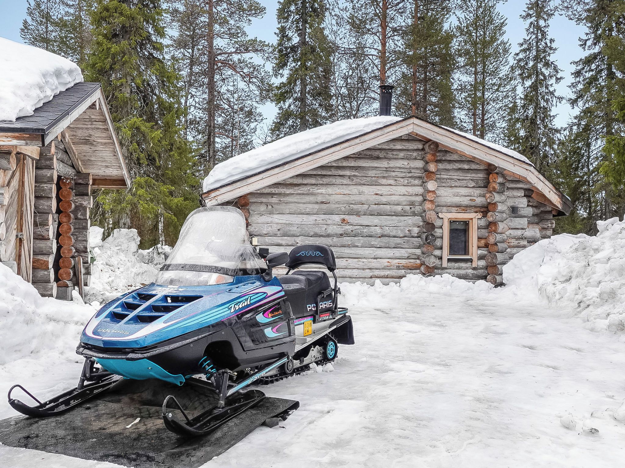 A snowmobile parked in front of a log cabin with a snow-covered roof and a chimney.