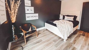 Moderni makuuhuone, jossa on sänky, tuoli, yöpöytä ja seinäkoristeita.