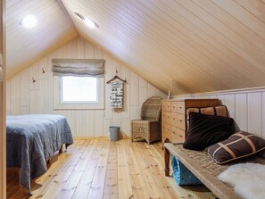 A cozy attic bedroom with a sloped ceiling, wooden walls, a window, a bed, a dresser, and a chair. - Peurakumpu by Interhome (Inari)