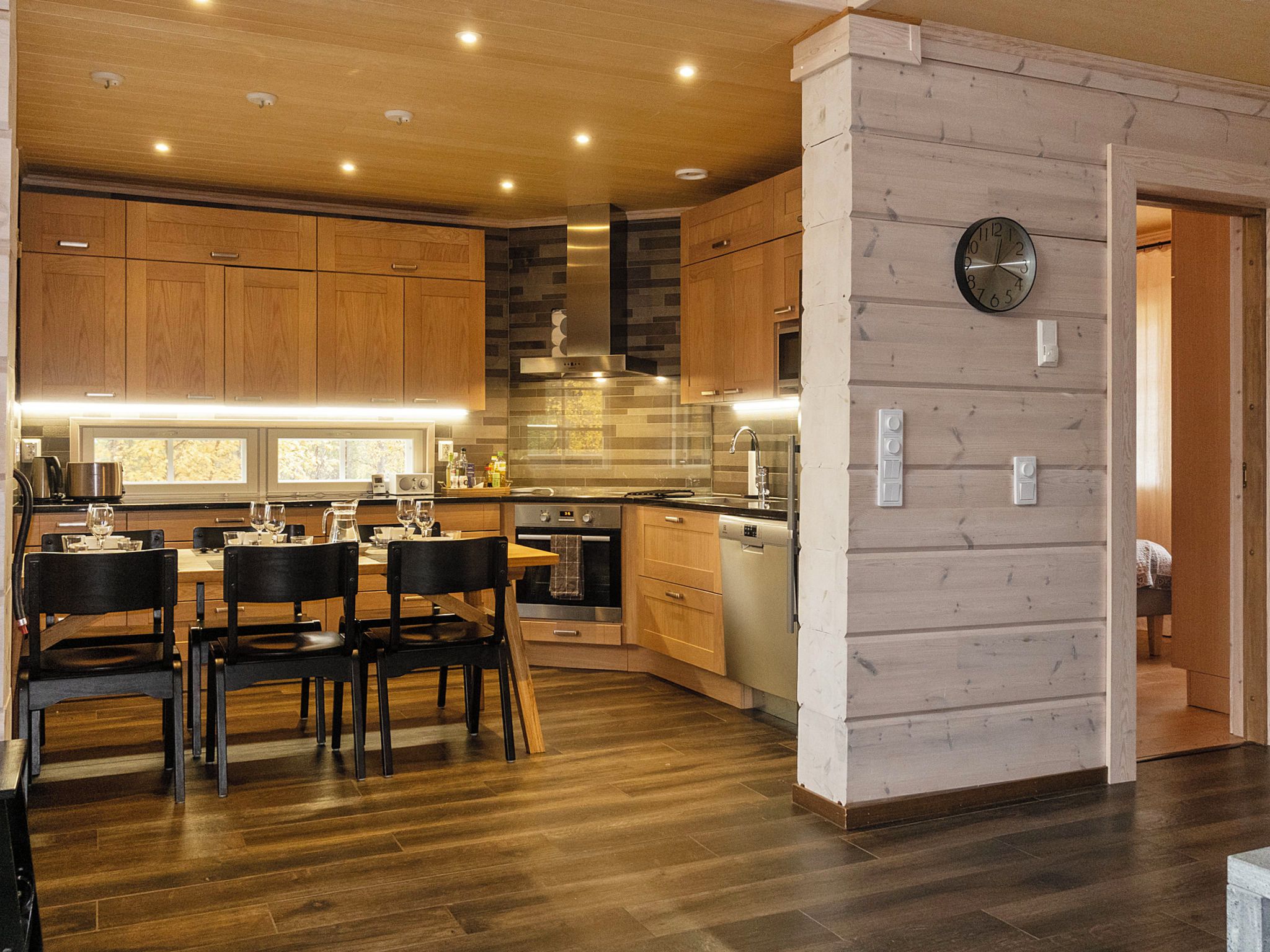 A modern kitchen with wooden cabinets, a built-in oven, and a dining area with a table and chairs.