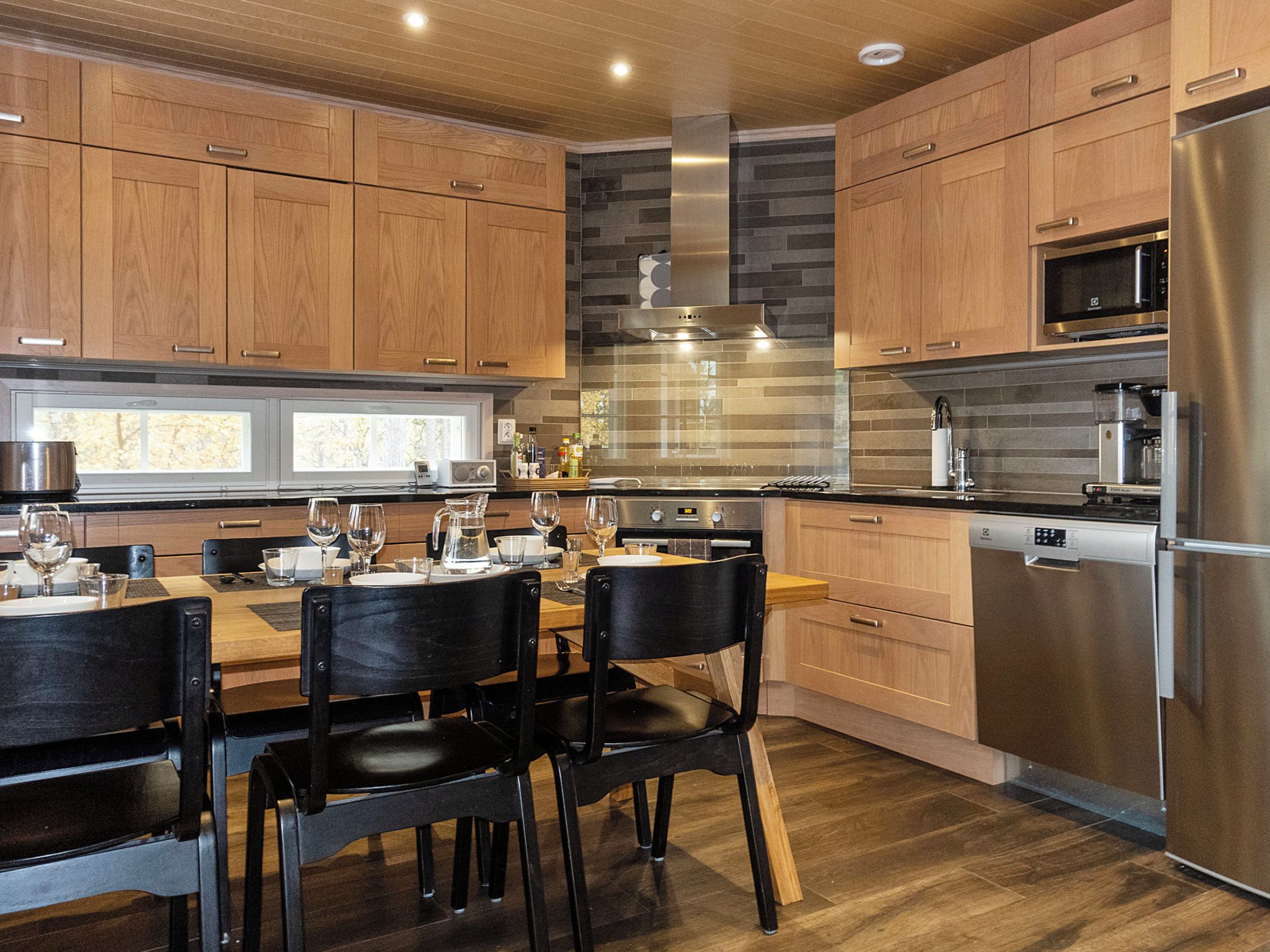 Une cuisine moderne avec des meubles en bois, un réfrigérateur en acier inoxydable et un coin repas avec une table dressée pour quatre personnes.