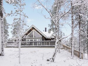 A log cabin with a large front porch, surrounded by snow-covered trees.
