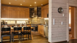 A modern kitchen with wooden cabinets, a dining area with a table and chairs, and a built-in oven. - Peurakumpu by Interhome (Inari)
