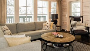 A cozy living room with a sofa, a round coffee table, and a chair. Large windows allow natural light and views of the outdoors. - Peurakumpu by Interhome (Inari)