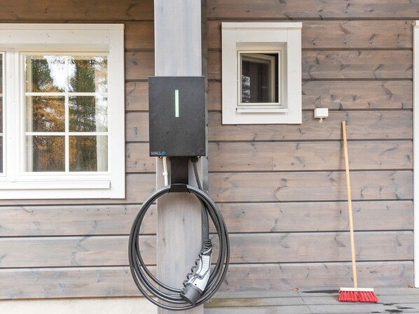 A utility box mounted on a wooden wall with a coiled cable and a broom leaning against the wall.