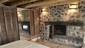 Una camera da letto con camino in pietra, persiane di legno e un letto con copripiumino bianco.