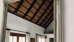 Una stanza con un grande specchio decorativo che riflette un divano bianco, un soffitto in legno e un quadro appeso al muro.