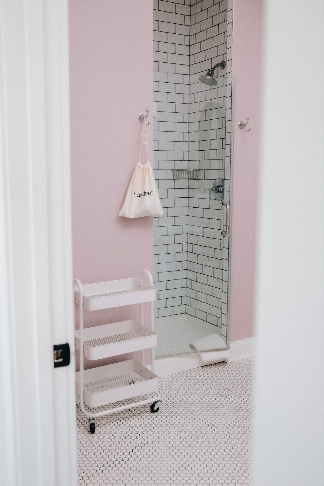 Un baño con ducha, una toalla blanca y un carrito de almacenamiento blanco.