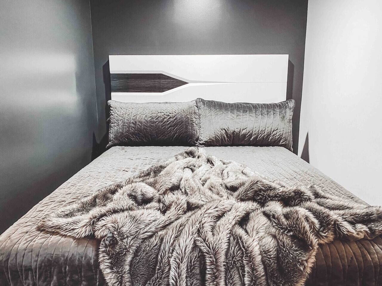 A bed with a textured blanket and a headboard with a geometric design.