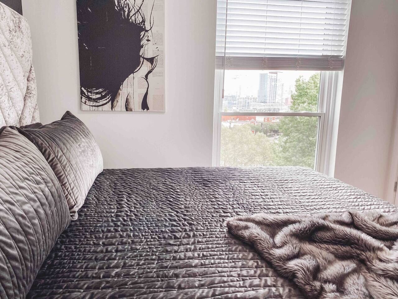 A bedroom with a bed, pillows, a blanket, and a window with blinds.