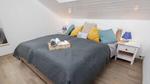 A neatly made bed with a grey quilt, a bedside table with a lamp, and a tray of folded towels. - Leuchtturm by Interhome (Norddeich)