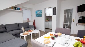 A modern living room with a grey sofa, a dining table set with food and drinks, and a kitchen in the background. - Leuchtturm by Interhome (Norddeich)