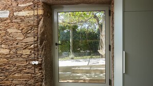 A stone wall adjacent to a door with a glass panel, a metal gate, and a concrete step leading to a driveway.