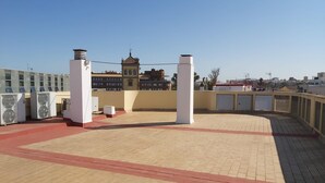 A rooftop terrace with a paved floor, two white pillars, and air conditioning units. - Misterhost San Bernardo (Sevilla)