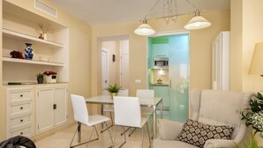 A modern living room with a sofa, chairs, a coffee table, and a dining area with a table and chairs. There is a kitchen visible through an open door. - Misterhost San Bernardo (Sevilla)