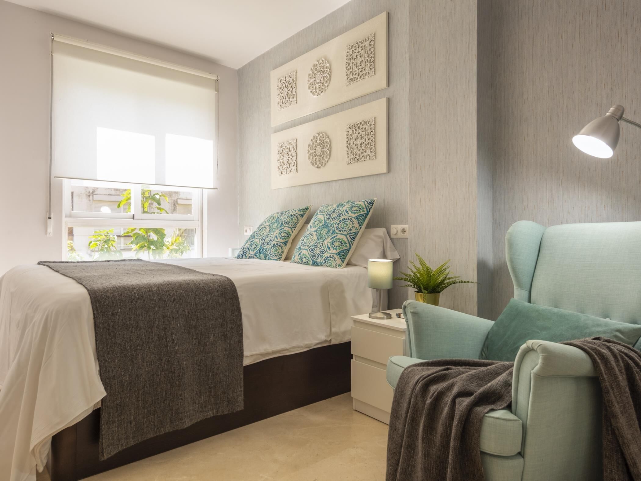 Een moderne slaapkamer met een bed, nachtkastje, lamp en decoratieve wandkunst.