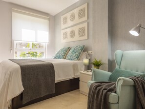 Een moderne slaapkamer met een bed, nachtkastje, lamp en decoratieve wandkunst.