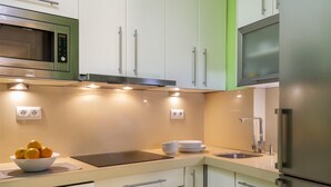 A modern kitchen with white cabinets, a stainless steel microwave, a built-in oven, and a refrigerator. There are two wall-mounted light fixtures and a sink with a faucet. - Misterhost San Bernardo (Sevilla)
