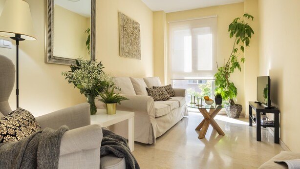 A modern living room with a sofa, a coffee table, a TV, and a large window. - Misterhost San Bernardo (Sevilla)