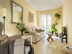 Ein modernes Wohnzimmer mit einer Couch, einem Couchtisch, einem Fernseher und einem großen Fenster.
