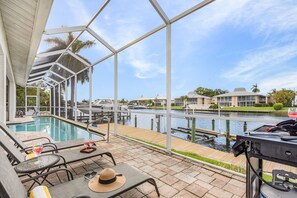 A poolside area with a grill, lounge chairs, and a view of a marina.