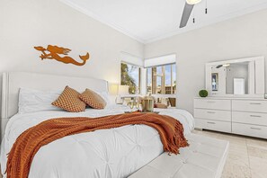 A bedroom with a large bed, a decorative mermaid wall art, a window with a view, and a modern dresser.