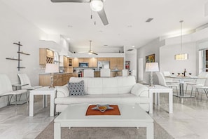 Een moderne woonkamer met een witte bank, salontafel en een eethoek met witte stoelen.