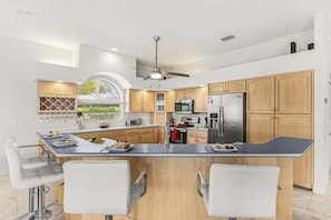 Una cocina moderna con una isla central, armarios de madera, electrodomésticos de acero inoxidable y un comedor con taburetes de bar.