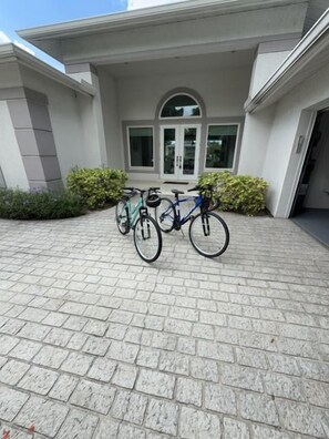 Entrada de un edificio con un camino pavimentado, dos bicicletas estacionadas afuera y un puerta de vidrio.