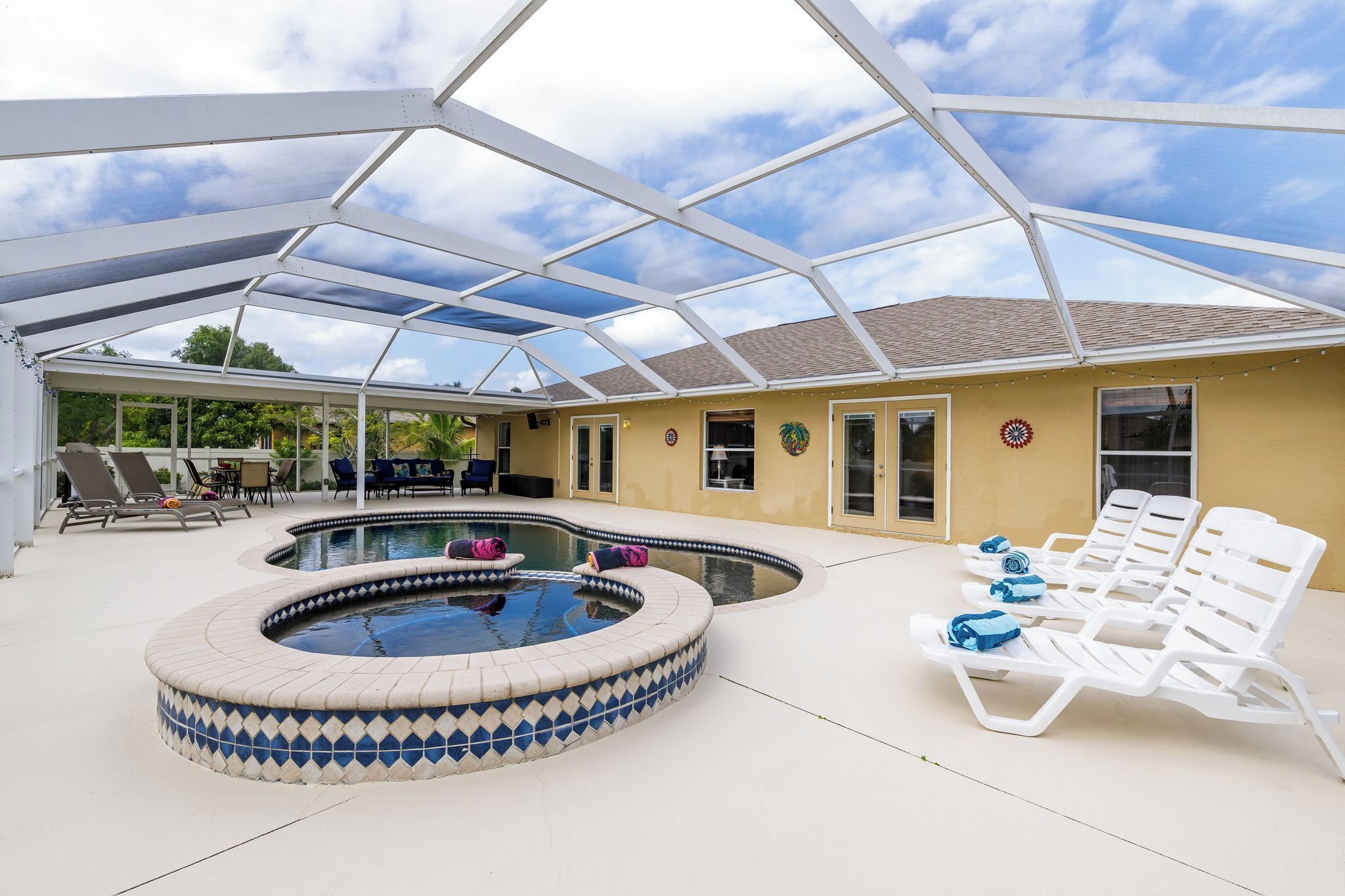 A covered swimming pool area with lounge chairs and a hot tub.
