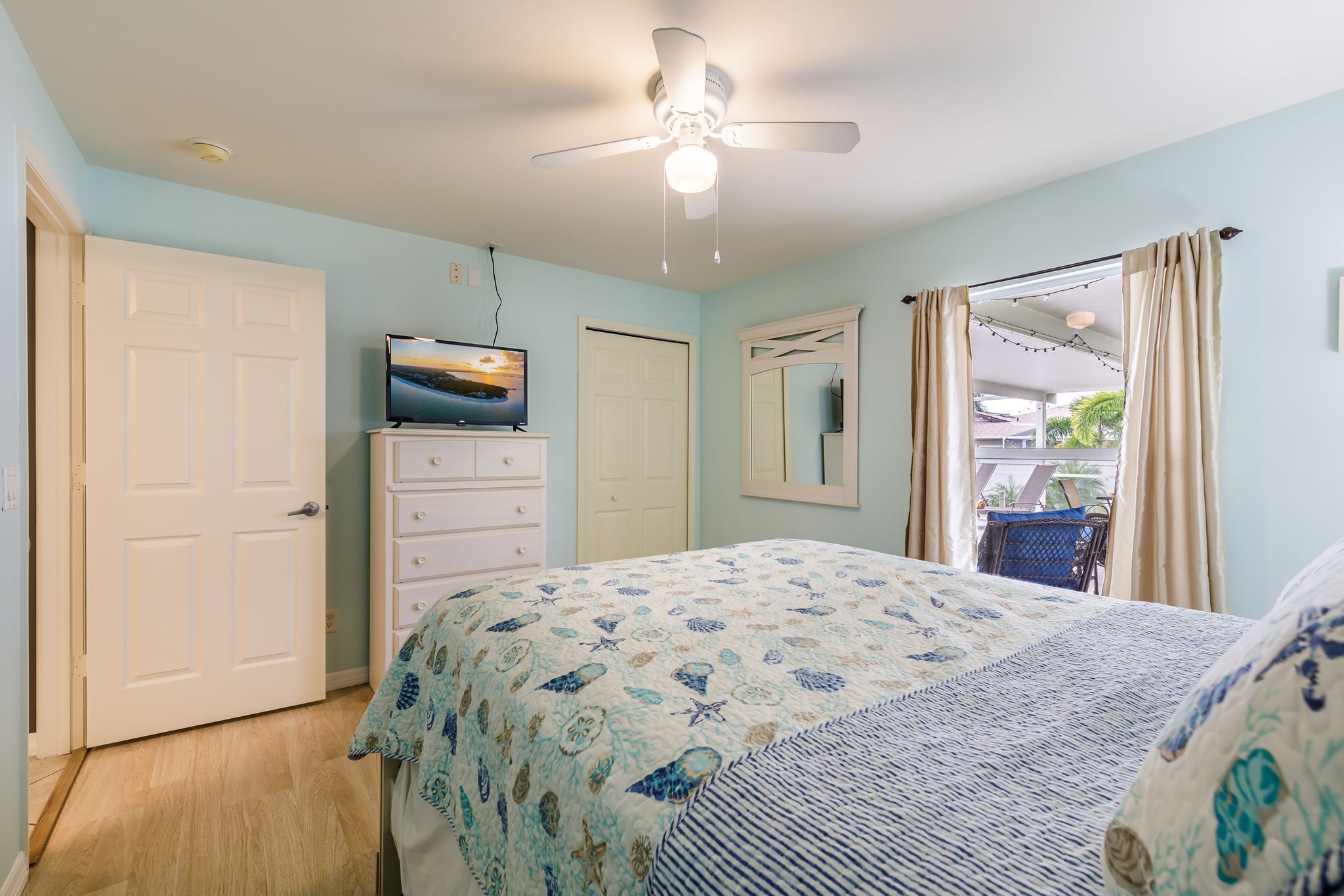 A bedroom with a bed, a ceiling fan, a TV on a dresser, and a window with curtains.