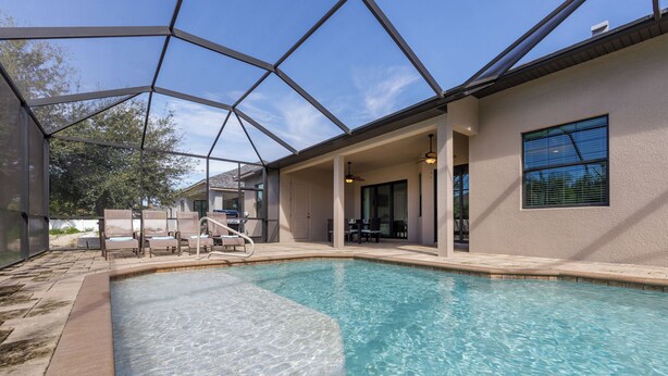A swimming pool with a glass ceiling, surrounded by lounge chairs and a covered patio area.