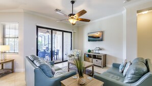 A modern living room with a ceiling fan, a sofa, a coffee table, and a TV mounted on the wall.