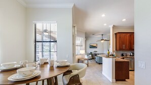 A modern kitchen with wooden cabinets, a dining area with white chairs, and a view of the living room.