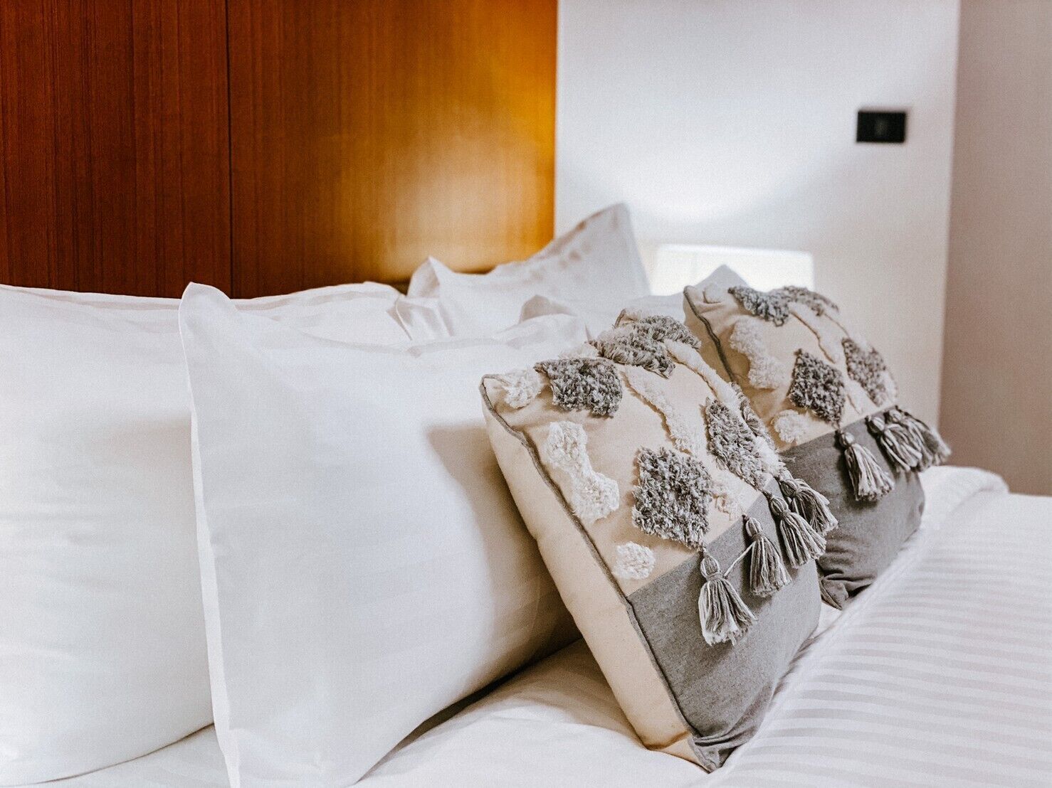 Una cama impecablemente tendida con sábanas blancas y almohadones decorativos con flecos.