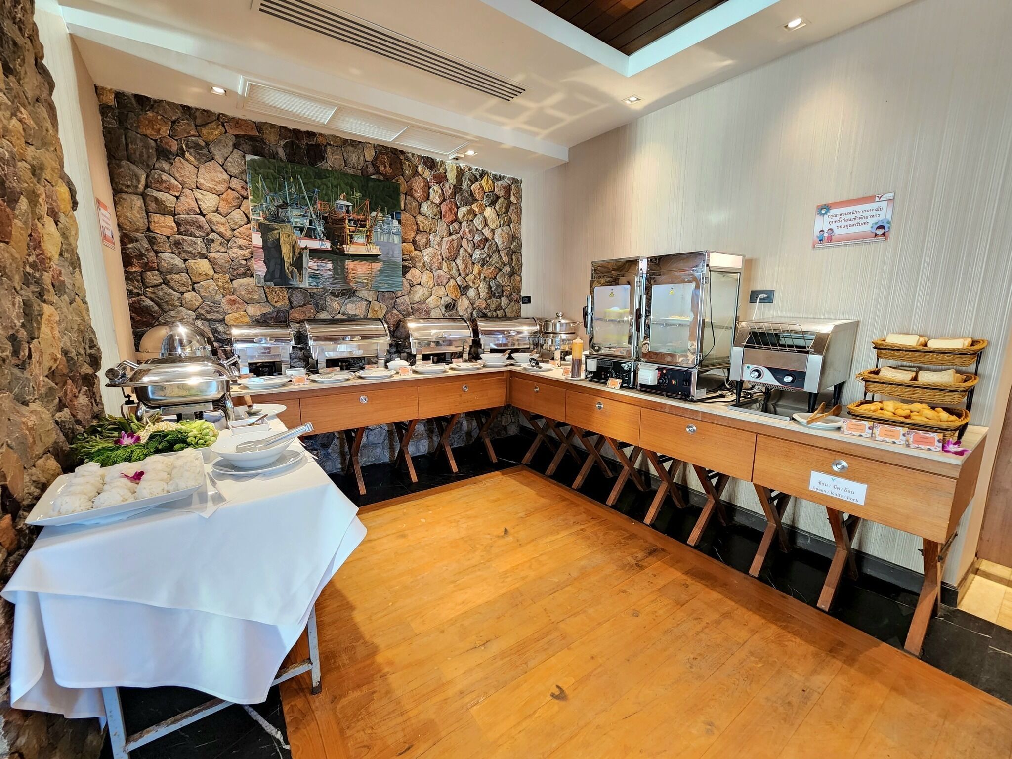 A buffet setup with multiple food stations, a stone wall backdrop, and a wooden table with a white tablecloth.