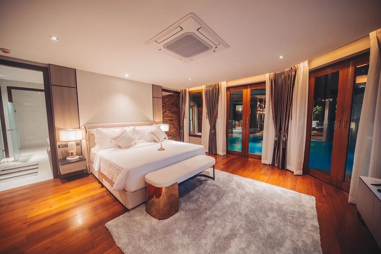 A modern bedroom with a large bed, a bedside table, a bench, and a view of a swimming pool through glass doors.